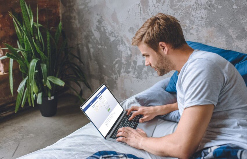young man in bed using laptop with facebook on screen