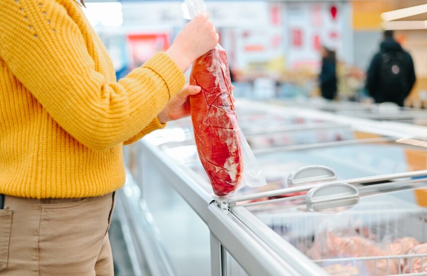 Close-up of a woman holding a piece of frozen meat in a store, a customer choosing food