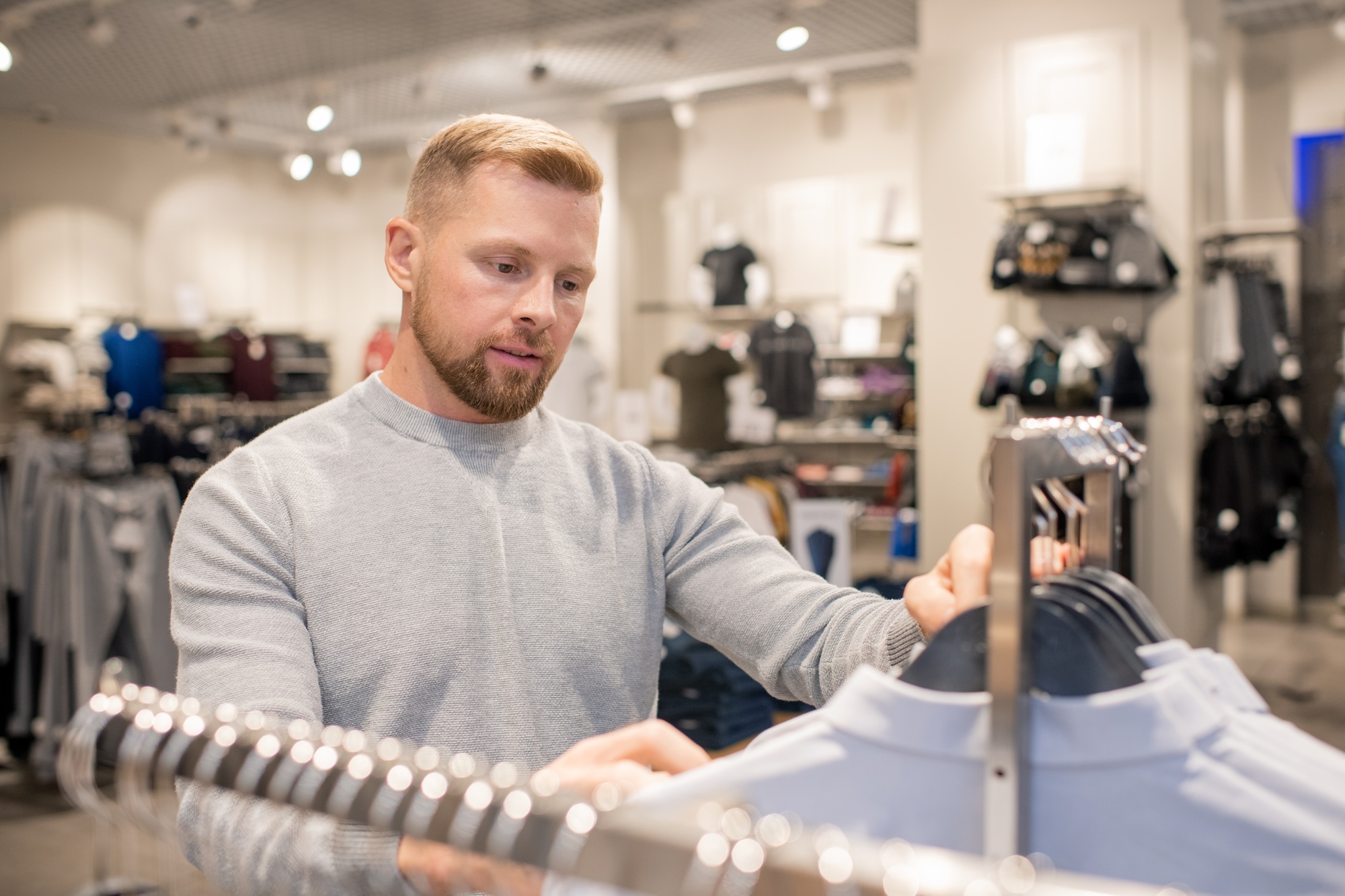 Young male shopper looking for his size while standing by rack with shirts